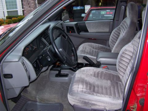 1994 Jeep Grand Cherokee - The interior of a red 1994 Jeep Grand Cherokee features gray velour seats and a dashboard with visible gauges.