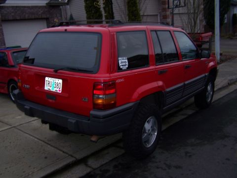 1994 Jeep Grand Cherokee - Rear view of a red Jeep Grand Cherokee, parked on a street next to another red vehicle.