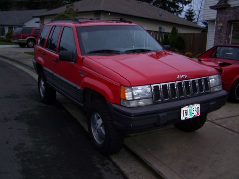 1994 Jeep Grand Cherokee - A red 1994 Jeep Grand Cherokee is parked on a driveway, with another vehicle visible to its right.