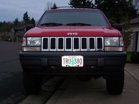 1994 Jeep Grand Cherokee - The front of a red Jeep Grand Cherokee is shown, with its distinctive grille and headlights visible.
