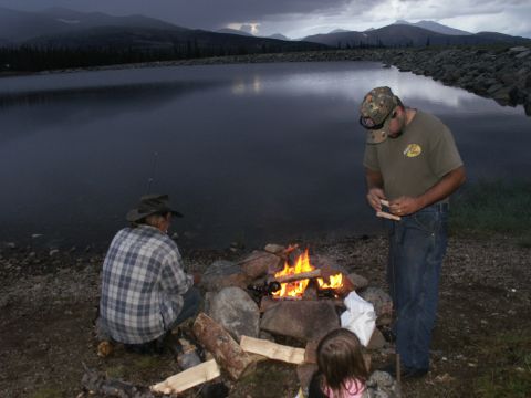 1995 Ford Bronco - A family enjoys a campfire and fishing by a calm lake at dusk.