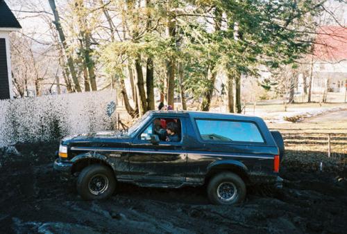 Black 1995 Ford Bronco in mud, side view with spare tire on rear