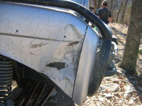 1992 Ford Mustang - Close-up of a damaged silver fender and black roll bar on an off-road vehicle, with a person in the background.