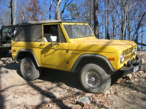 1992 Ford Mustang - A yellow Ford Bronco is parked on a rough, outdoor trail with trees in the background.