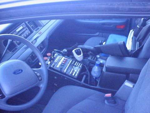 2002 Ford Crown Victoria - The interior of a police vehicle features a steering wheel, dashboard, and a console equipped with communication devices.