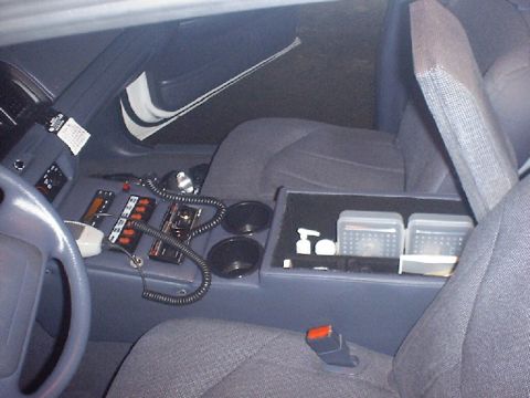 2002 Ford Crown Victoria - The console area of a police vehicle is equipped with communication devices and storage compartments.