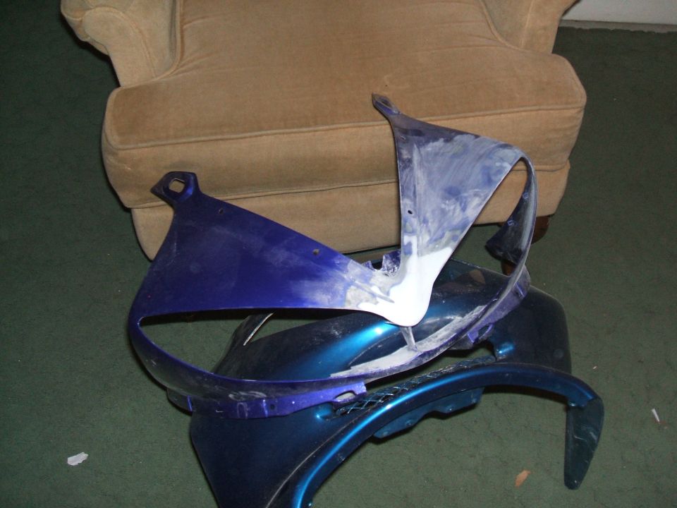 Pile of blue and white motorcycle fairing pieces on the floor next to a chair