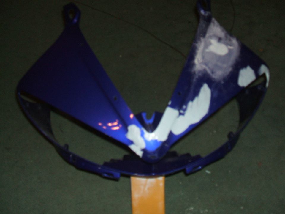 Blue motorcycle fairing with white primer spots, mounted on an orange stand