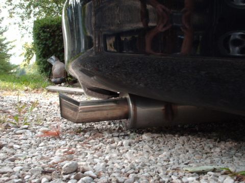 1995 Ford Probe - The rear of a dark-colored vehicle is shown, focusing on the exhaust pipe and bumper, with a raccoon statue nearby.