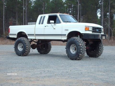 1990 Ford F-150 - This heavily modified Ford pickup truck features oversized tires and a significant lift kit, giving it an aggressive stance.