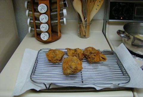 1989 Ford Bronco - Freshly fried chicken rests on a wire rack, draining on paper towels, with kitchen utensils and spices visible.