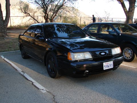 1993 Ford Taurus - A black 1993 Ford Taurus is parked in a lot, showing its front grille and license plate.