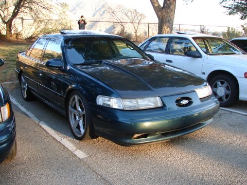 1993 Ford Taurus - A dark green sedan is parked in a lot with another vehicle beside it. The car has a sunroof and aftermarket wheels.