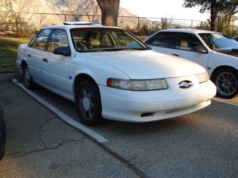 1993 Ford Taurus - A white sedan is parked in a lot next to another white vehicle.