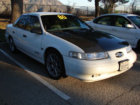 1993 Ford Taurus - A white sedan with a black hood and aftermarket wheels is parked next to another white vehicle.