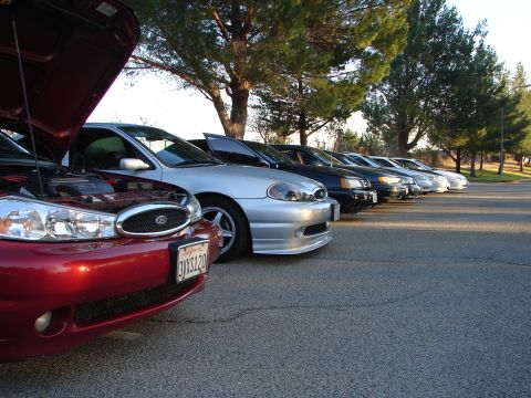 1993 Ford Taurus - A line of cars, including a red car with its hood open and a silver car, are parked in a lot.