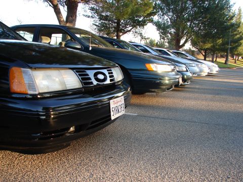 1993 Ford Taurus - A line of cars, including a black Ford Taurus, are parked in a lot during the day.