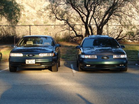 1993 Ford Taurus - Two dark green Ford Taurus sedans are parked in a lot, with one on the left displaying a license plate.