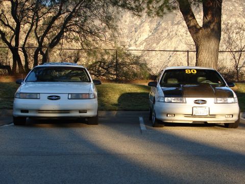 1993 Ford Taurus - Two 1993 Ford Taurus sedans are parked in a lot, one with a modified black hood and a yellow '80' sticker on the windshield.