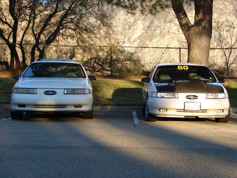 1993 Ford Taurus - Two Ford Taurus sedans, one with a custom hood and '80' sticker, parked outdoors.