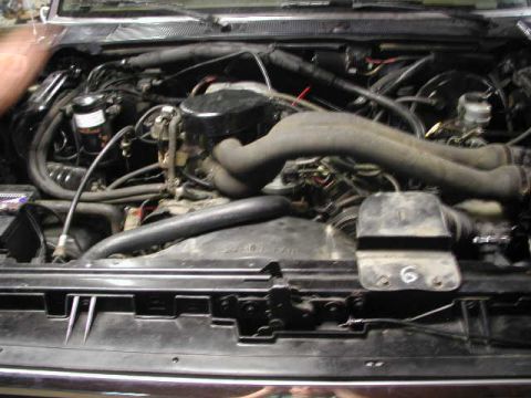 1988 Ford F-150 - The engine compartment of a vehicle is shown, with various mechanical parts and hoses.