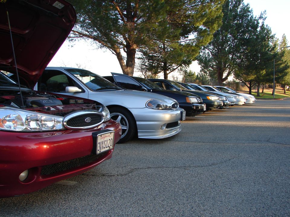 Red sedan with hood open, parked in a line with other sedans