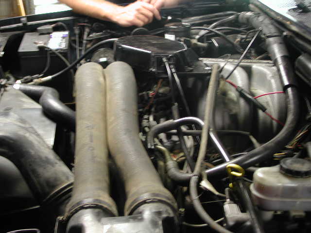 Engine bay with two large intake hoses in the foreground, battery on the left, and various engine components