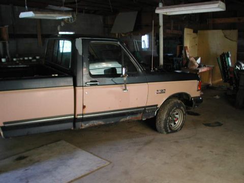 1988 Ford F-150 - A two-tone Ford pickup truck is parked inside a garage with various items in the background.