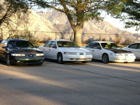 1991 Ford Taurus - Three Ford Taurus sedans are parked in a lot with mountains in the background.