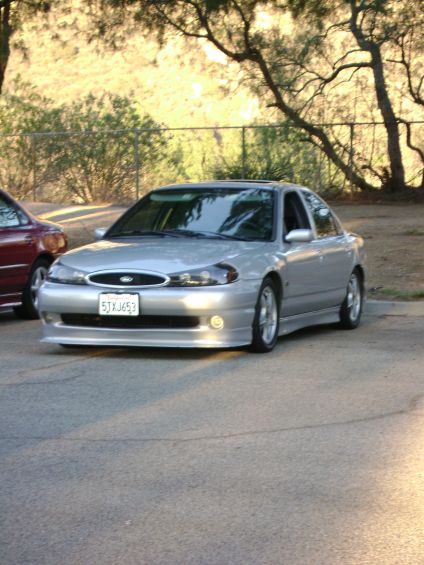 1991 Ford Taurus - Silver sedan with aftermarket body kit parked outdoors next to another vehicle.