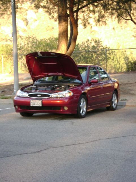 1991 Ford Taurus - A red sedan is parked outdoors with its hood raised, revealing the engine compartment.
