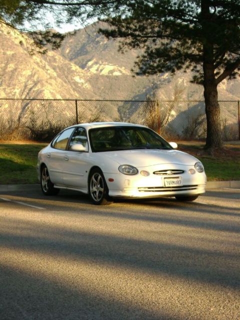 1991 Ford Taurus - White sedan with a license plate WRM683 parked outdoors with mountains in the background.