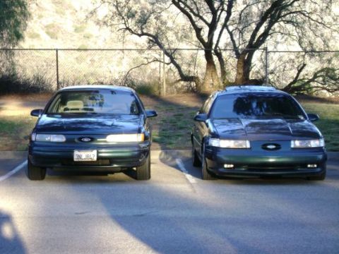 1991 Ford Taurus - Two dark green 1991 Ford Taurus sedans are parked side-by-side, viewed from the front.