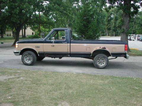 1988 Ford F-150 - This two-tone Ford F-150 pickup truck is seen from the side, with visible rust on the rear fender.