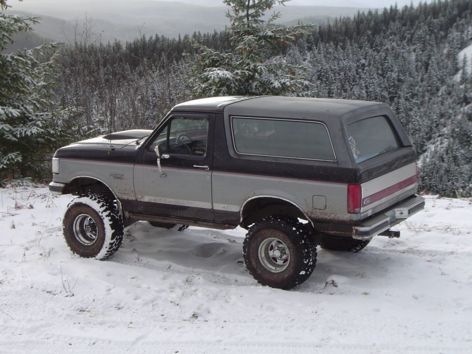 Lifted black and silver Ford Bronco parked in snow overlooking evergreen mountains