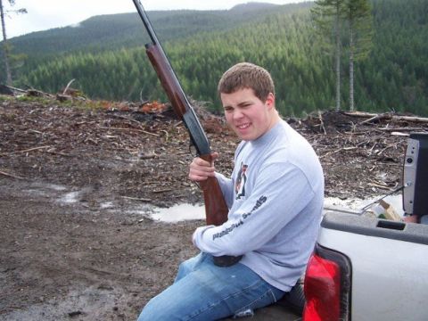 1993 Ford Bronco - A young man sits in the bed of a pickup truck, holding a shotgun, with a wooded hillside behind him.