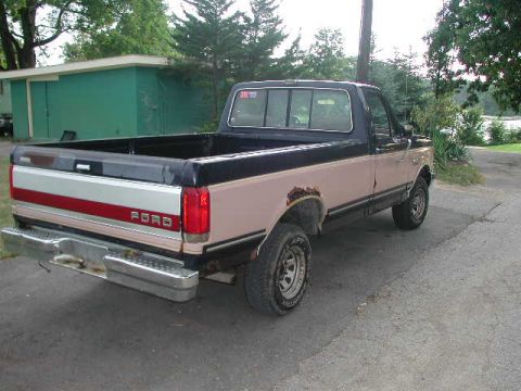 1988 Ford F-150 - This pickup truck, identified as a 1987 Ford F-150, is parked on an asphalt surface near a body of water.