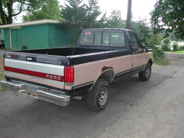 Two-tone brown and black Ford F-150 pickup truck with rust spots, seen from the rear three-quarter angle