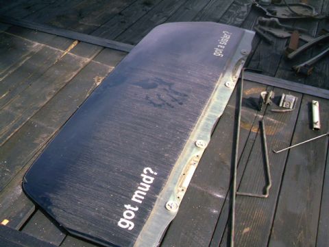 1989 Ford Bronco - A detached car door with decals sits on a wooden deck alongside various metal parts and tools.