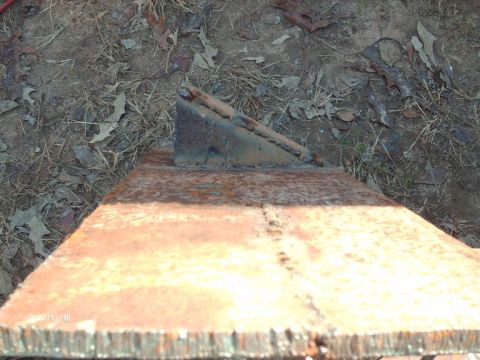 1990 Ford F-150 - A close-up view of a rusty metal bracket, likely a vehicle part, resting on a metal plate outdoors.
