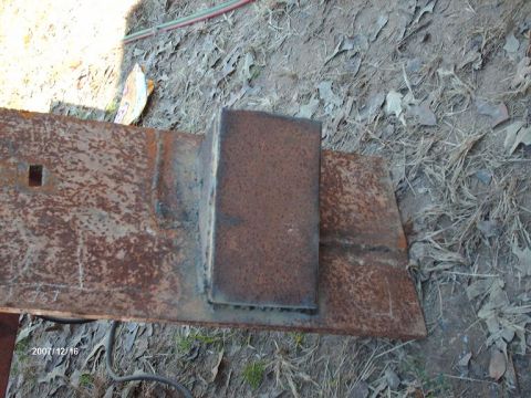 1990 Ford F-150 - A close-up view of a rusty metal bracket, likely a custom part for a vehicle modification, showing a square hole and a welded block.