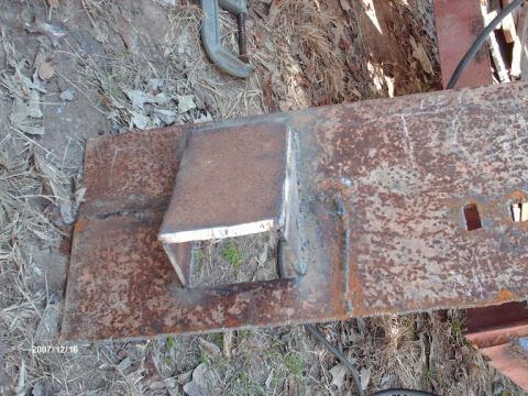 1990 Ford F-150 - Close-up of a fabricated metal bracket welded onto a rusty steel plate, with a clamp visible.