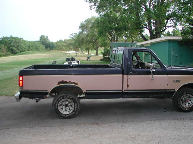 Side view of a two-tone 1988 Ford F-150 pickup truck with rust on the rear fender