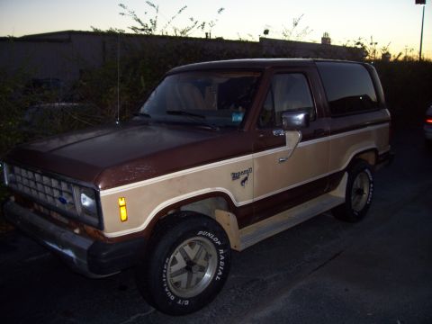 1984 Ford Bronco II - A two-door Ford Bronco II is parked outdoors at dusk, showing its two-tone paint scheme and side profile.