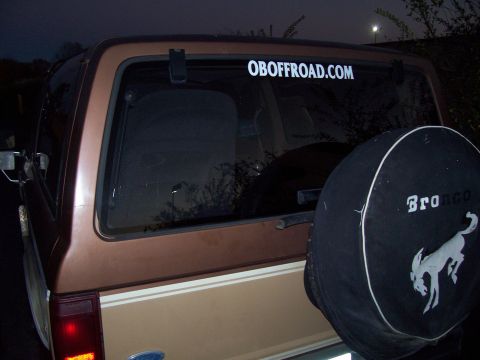 1984 Ford Bronco II - The rear of a 1984 Ford Bronco II is shown with a spare tire cover and a website sticker on the window.