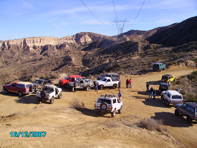 Group of SUVs and trucks parked on a dirt road with mountains in the background. 1990 Ford Bronco visible