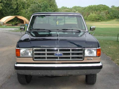 1988 Ford F-150 - This dark blue pickup truck features a prominent chrome grille and a tan accent on its lower front fascia.