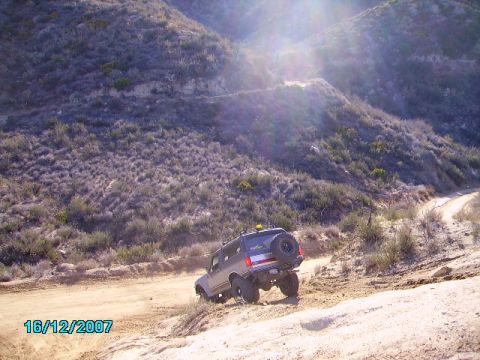 1990 Ford Bronco - A Ford Bronco navigates a steep, dusty trail under a bright, sunlit sky.