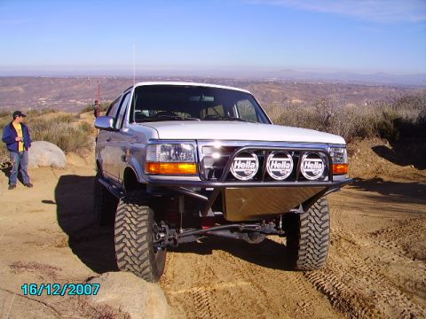 1990 Ford Bronco - A modified Ford F-Series truck is parked on a dirt trail with a scenic overlook in the background.