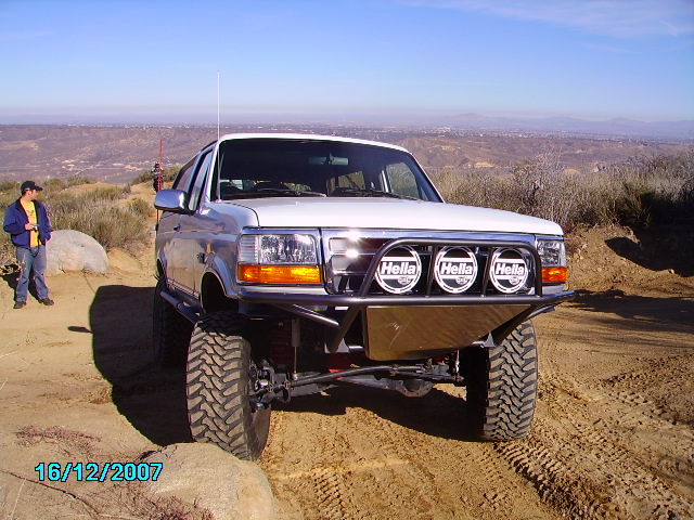 White Ford F-Series truck with aftermarket bumper and Hella lights on a dirt trail